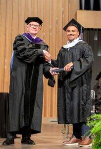 MLS Student in Regalia receiving Diploma Tube from Dean Halvorson