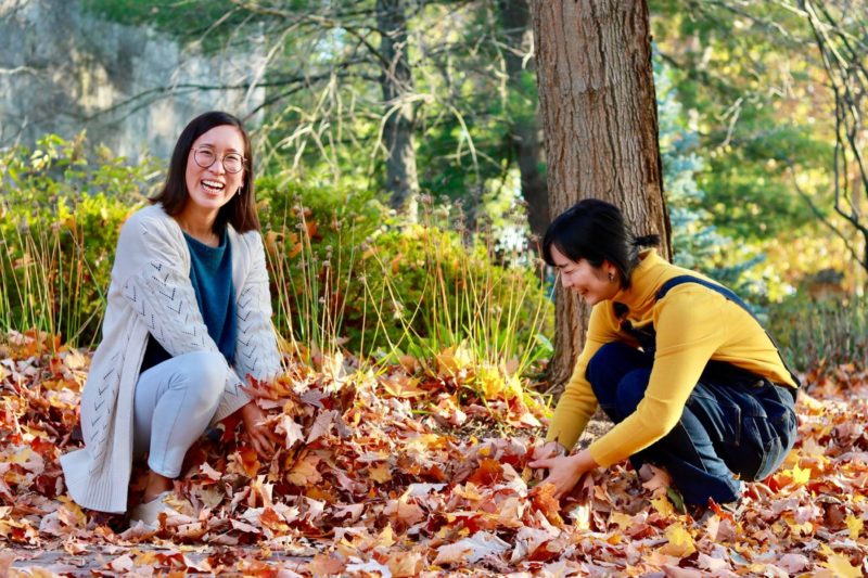 Photograph of Moe Higa and Hanna Kim sitting in fall leaves.