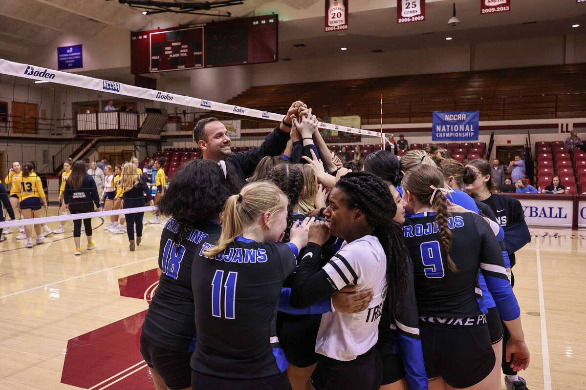 Volleyball team huddles with hands in the air. 