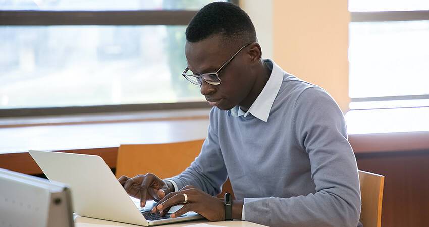student typing on computer at the library